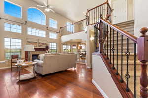 Living room with arched walkways, a ceiling fan, hardwood / wood-style flooring, a towering ceiling, and baseboards