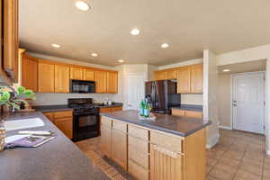 Kitchen featuring black appliances, recessed lighting, dark countertops, a kitchen island, and light tile patterned floors