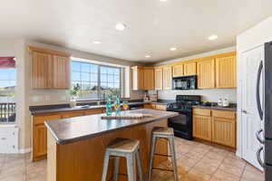 Kitchen with black appliances, dark countertops, light tile patterned floors, a kitchen island, and a kitchen bar