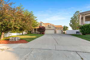 View of property hidden behind natural elements with an attached garage, concrete driveway, and stucco siding