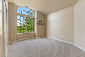 Spare room featuring light carpet, lofted ceiling, and baseboards