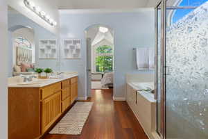 Ensuite bathroom featuring a garden tub, hardwood / wood-style floors, double vanity, a shower stall, and baseboards