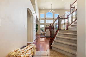Tiled foyer featuring ceiling fan, arched walkways, stairway, baseboards, and a high ceiling