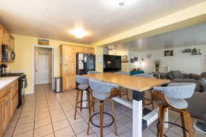 Kitchen featuring black appliances, open floor plan, light brown cabinets, and light tile patterned floors