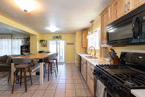 Kitchen with black appliances, a sink, light countertops, and plenty of natural light