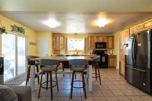 Kitchen featuring black appliances, light tile patterned floors, a sink, light countertops, and a breakfast bar