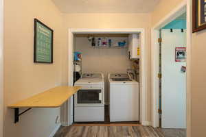 Laundry area with washer and clothes dryer, water heater, wood finished floors, and a textured ceiling