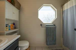 Bathroom featuring tile patterned flooring, vanity, toilet, baseboards, and a shower with curtain