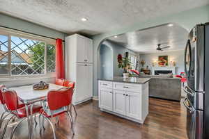 Kitchen with freestanding refrigerator, a textured ceiling, arched walkways, a ceiling fan, and dark wood-style flooring