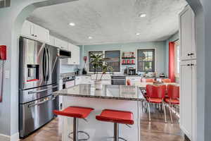 Kitchen featuring appliances with stainless steel finishes, arched walkways, dark wood finished floors, a textured ceiling, and white cabinets