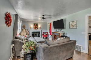 Living room with a textured ceiling, baseboards, wood finished floors, ceiling fan, and a tile fireplace