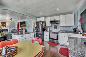 Kitchen with stainless steel appliances, a sink, arched walkways, dark wood-type flooring, and white cabinetry
