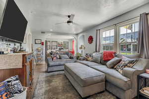 Living room with arched walkways, a textured ceiling, ceiling fan, dark wood-type flooring, and a bar