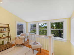 Living area with lofted ceiling, plenty of natural light, wood finished floors, and an upstairs landing