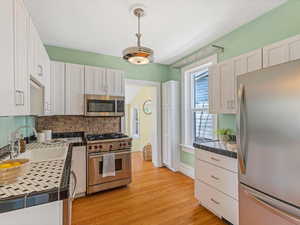 Kitchen featuring appliances with stainless steel finishes, a sink, white cabinetry, backsplash, and light wood-style flooring