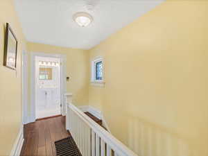 Hallway with an upstairs landing, dark wood finished floors, a textured ceiling, a sink, and baseboards