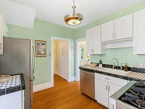 Kitchen with stainless steel appliances, a sink, tile countertops, baseboards, and white cabinets
