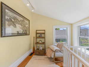 Sitting room with plenty of natural light, light wood finished floors, lofted ceiling, rail lighting, and baseboards