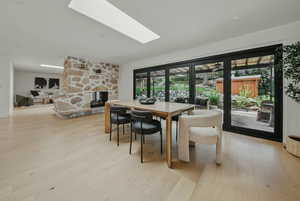 Dining area featuring a stone fireplace, a skylight, and light wood-style flooring
