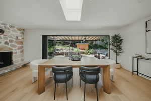Dining room with healthy amount of natural light, a fireplace, light wood-type flooring, and a skylight