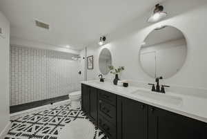 Full bath featuring toilet, double vanity, tiled shower, and tile patterned floors