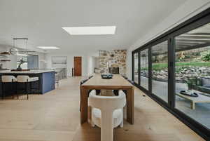 Dining room featuring a skylight, healthy amount of natural light, a stone fireplace, and light wood-style floors