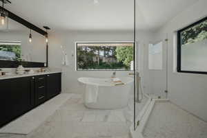 Full bath with plenty of natural light, double vanity, a freestanding tub, tile walls, and marble look tile flooring