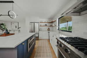 Kitchen with appliances with stainless steel finishes, wall chimney range hood, open shelves, a sink, and white cabinetry