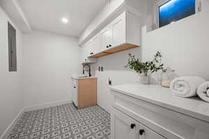 Washroom with light flooring, cabinet space, hookup for an electric dryer, electric panel, and baseboards