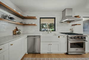 Kitchen featuring appliances with stainless steel finishes, open shelves, island range hood, a sink, and light wood-style floors