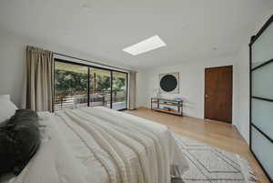 Bedroom featuring a skylight, light wood-style flooring, and access to outside