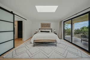 Bedroom featuring access to outside, a skylight, a barn door, light wood-style floors, and baseboards