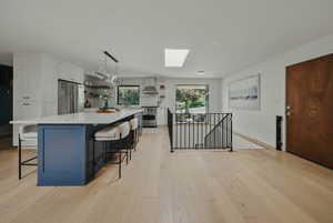 Kitchen featuring appliances with stainless steel finishes, open shelves, wall chimney range hood, a skylight, and white cabinetry