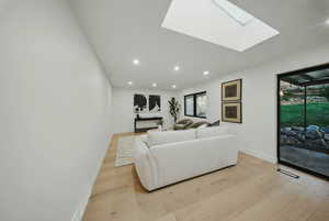 Living room with light wood-style floors, recessed lighting, baseboards, and a skylight
