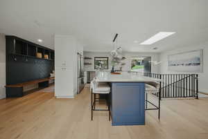 Kitchen with stainless steel appliances, open shelves, a skylight, white cabinets, and a breakfast bar area