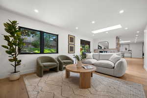 Living area featuring a skylight, light wood-style floors, baseboards, and recessed lighting