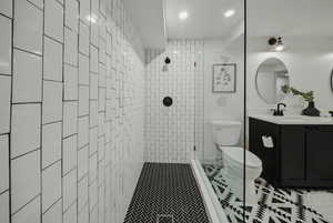 Bathroom with toilet, vanity, a tile shower, tile patterned floors, and recessed lighting