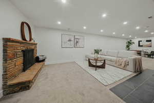 Living room featuring a fireplace with raised hearth, recessed lighting, light colored carpet, and baseboards