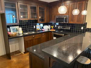 Kitchen featuring appliances with stainless steel finishes, backsplash, glass-fronted cabinets, a peninsula and a breakfast bar
