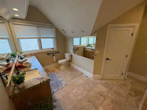 Primary bathroom up with lofted ceiling, travertine flooring and door to closet under the stairs