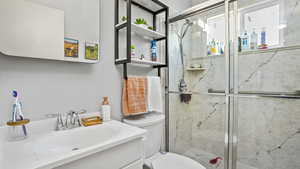 Full bath with a marble finish shower, vanity, and toilet