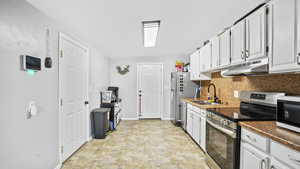 Kitchen with stainless steel appliances, under cabinet range hood, a sink, tasteful backsplash, and baseboards