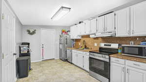 Kitchen with stainless steel appliances, a sink, under cabinet range hood, and white cabinetry