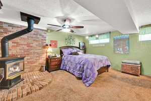 Carpeted bedroom with a fierplace, a textured ceiling, multiple windows, ceiling fan, and a textured wall