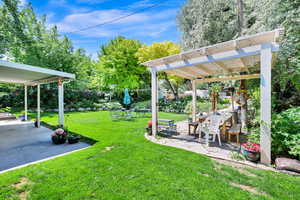 View of green lawn featuring a pergola, stone pavers in the patio area surrounded by mature trees