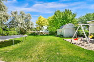 View of green lawn featuring a trampoline and a playground/sandbox