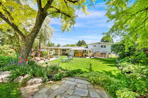 View from the terraced area of the backyard with green lawn featuring a patio, a pergola, and ample perennial plants