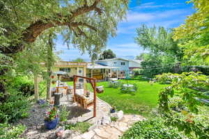View of grassy yard featuring a stone paver patio and an outdoor living space surrounded with mature trees