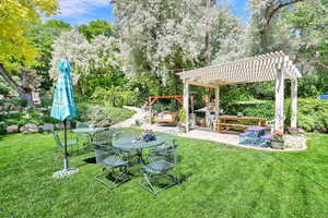 View of green lawn featuring a pergola, stone pavers in the patio area surrounded by mature trees