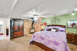 Bedroom featuring a wood stove, light carpet, a textured ceiling, and ceiling fan